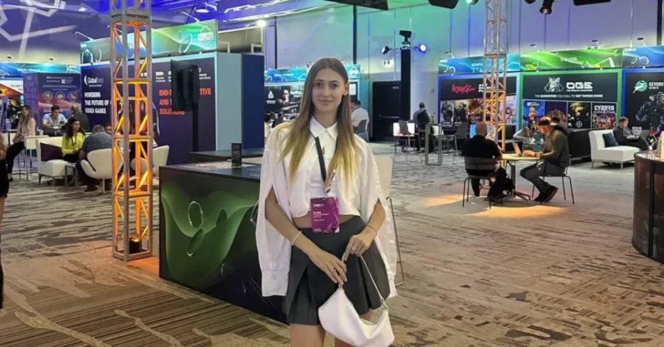 Conference attendee standing among game industry exhibition booths, tables and visitors.